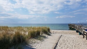 A sandy beach with a wooden pier extending into the water, a clear sky, and a calm sea.