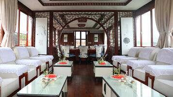 A traditional-style room with a central dining area, two sofas, and a table with a vase and fruit.