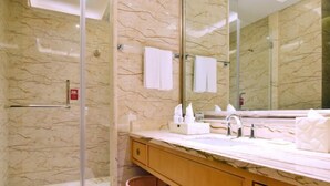 Un baño con pared de mármol, un lavamanos con espejo, un perchero y un cesto de basura.