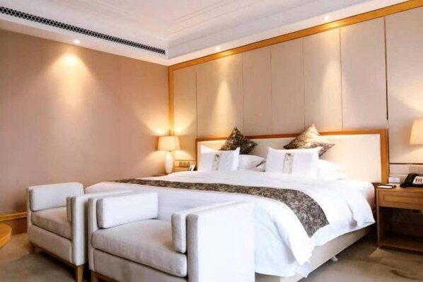 A hotel room with a large bed, two armchairs, a nightstand, and a wall-mounted lamp.