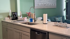 Una cocina equipada con lavavajillas, cafetera y pileta. Hay un cuadro en la pared y una lámpara al fondo.