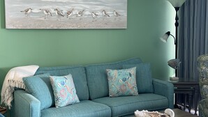 Un sofá azul aguamarina con cojines estampados, un cuadro abstracto de gran tamaño, una lámpara de pie y una mesita con objetos decorativos.