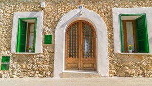 A stone building with a wooden door and green shutters.