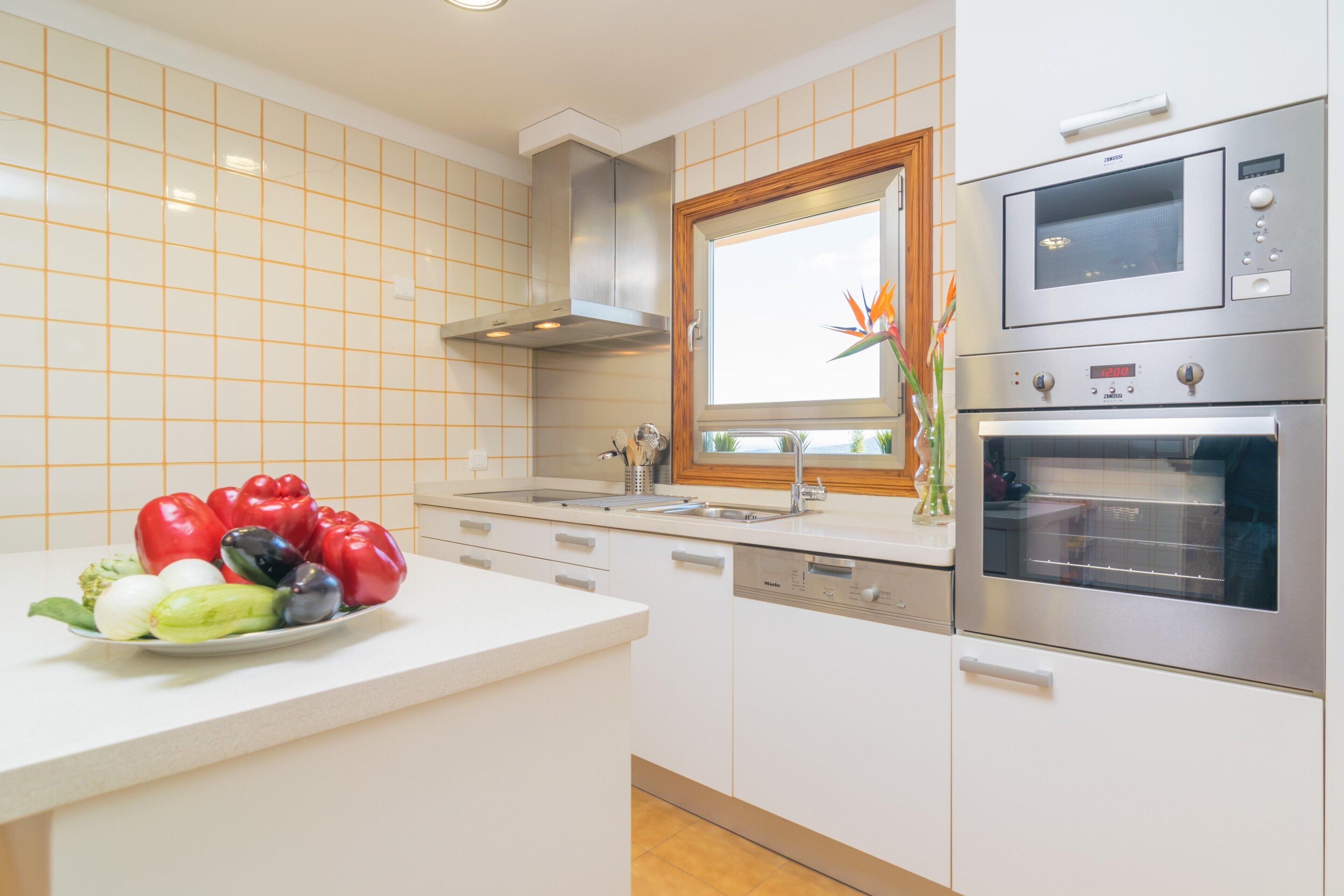 Una cocina moderna con armarios blancos, electrodomésticos de acero inoxidable y un ventanal sobre el fregadero.