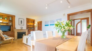A spacious living room with a wooden dining table, white chairs, a fireplace, and a television.