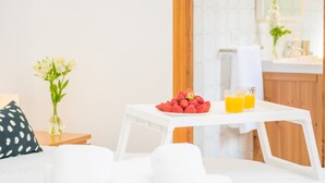 A neatly arranged breakfast table with a bowl of strawberries and two glasses of orange juice, a white chair, and a small table with a vase of flowers.