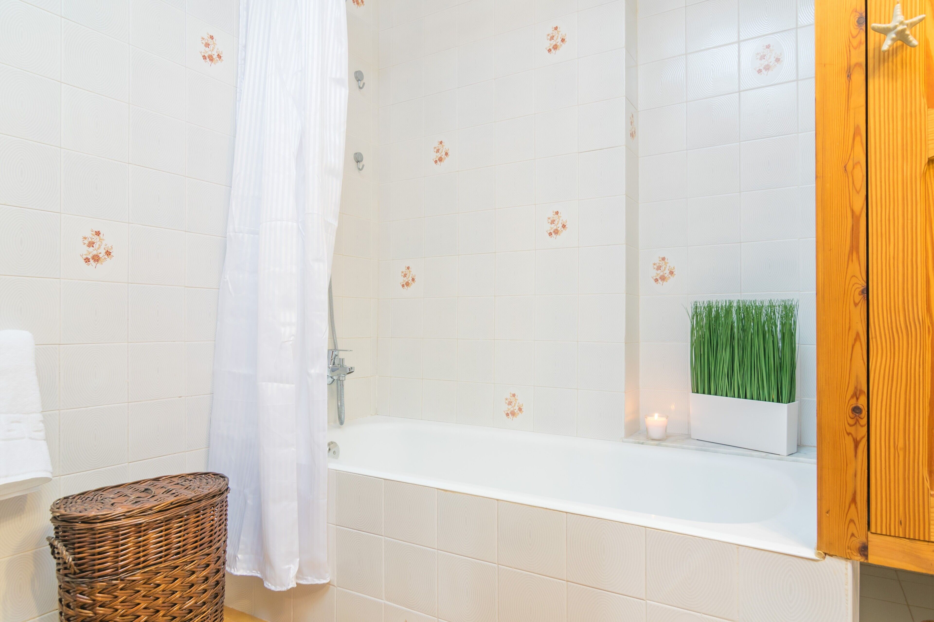Une salle de bain avec une baignoire, un panier en osier, un rideau blanc et une petite plante accrochée au mur.