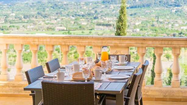 A dining table set for breakfast with a scenic view of a lush valley and mountains in the background.