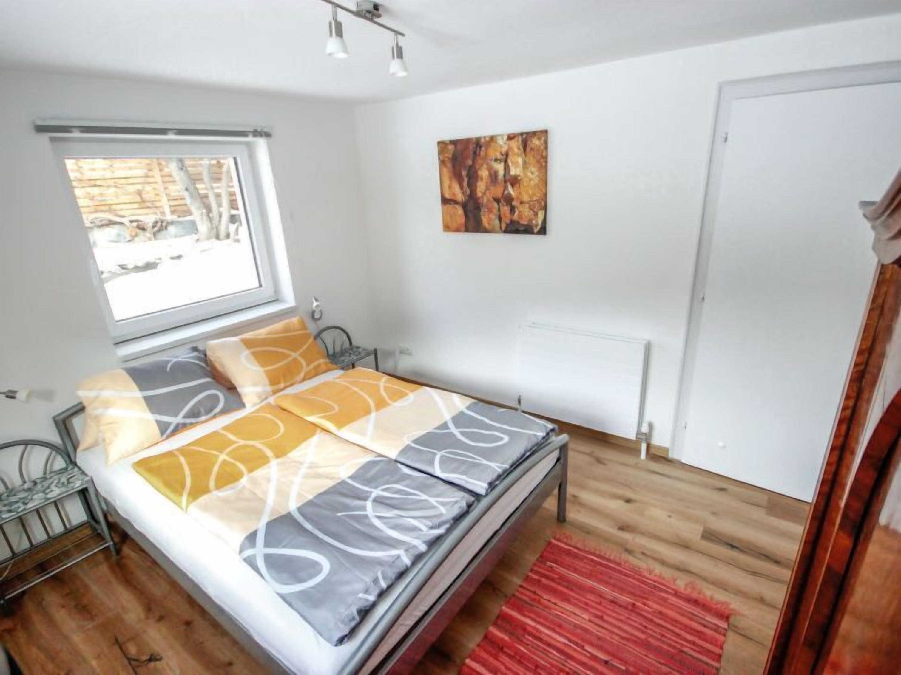 A bedroom with a bed, a window, a radiator, and a door.