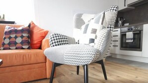 A modern living room with a sofa, patterned armchair, and a kitchen area with cabinets and an oven. - Apartment Stein by Interhome (Pians)