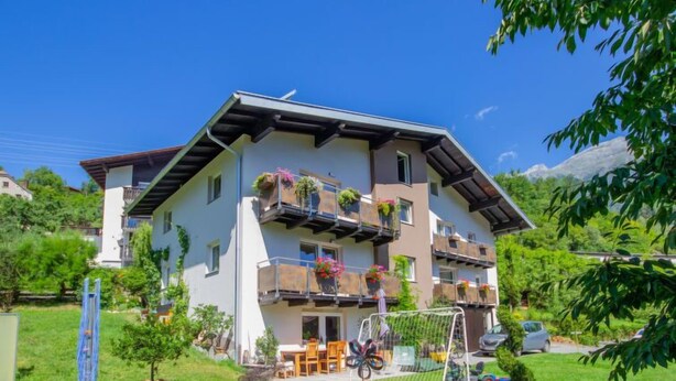 A two-story building with balconies, a small garden, and a mountain in the background. - Apartment Stein by Interhome (Pians)