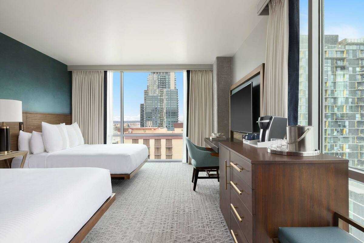 Habitación de hotel con dos camas, un escritorio, un televisor y vista a la ciudad.