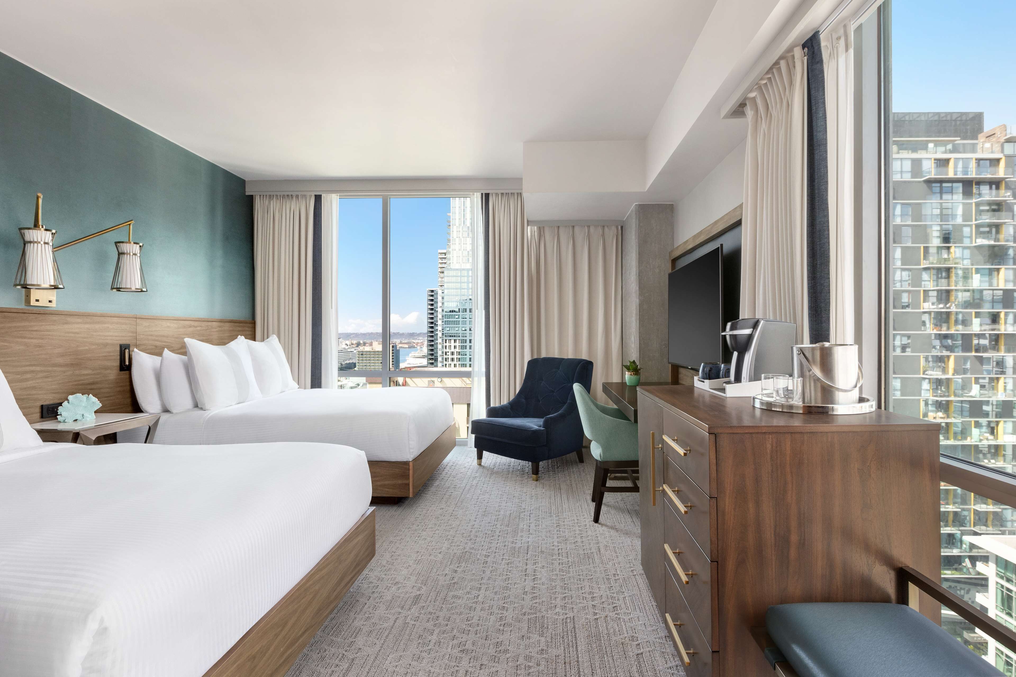 A hotel room with two beds, a desk, a TV, and a city view.