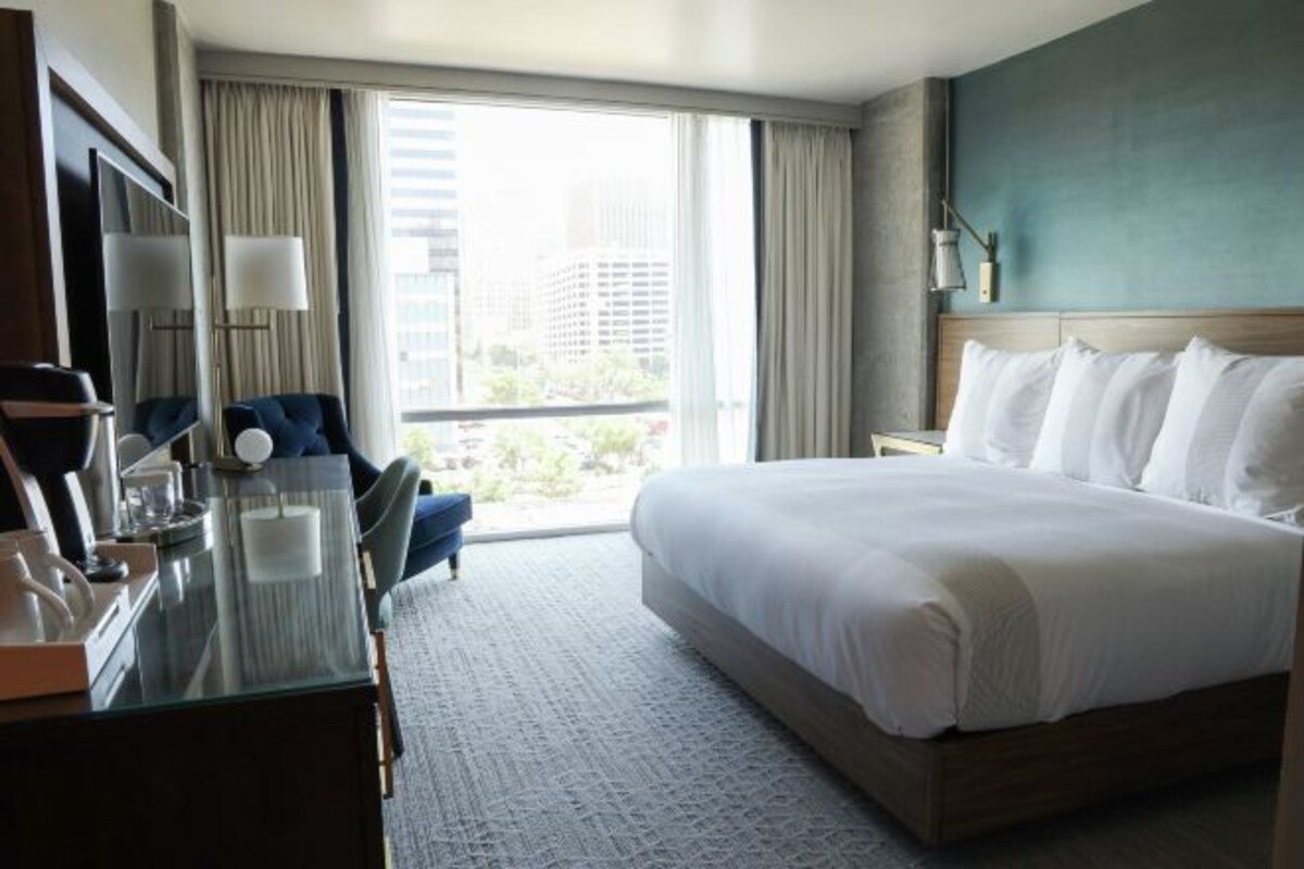 Habitación de hotel con una cama grande, un escritorio con silla, televisión y ventana con cortinas.