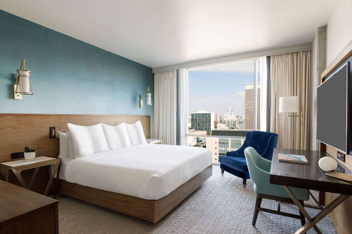 Una habitación de hotel con una cama grande, un escritorio con silla, televisión y vistas a la ciudad.