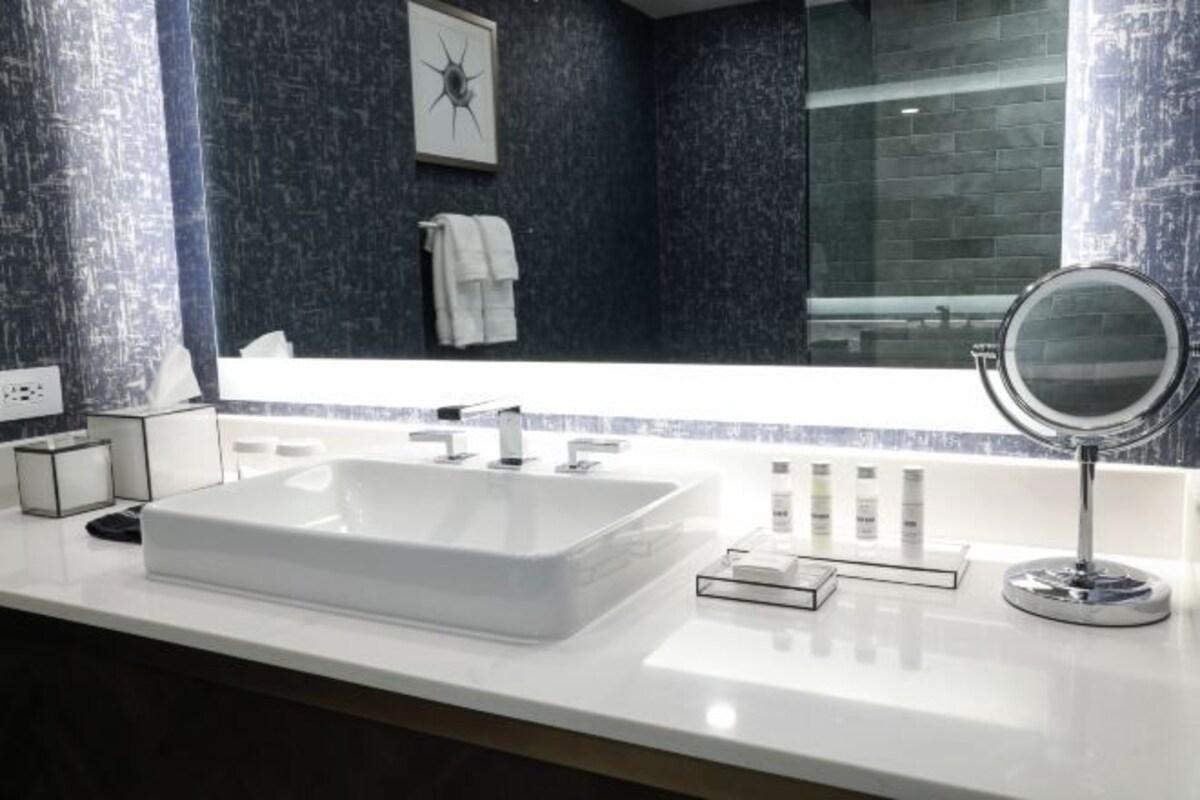 A modern bathroom with a large white sink, a mirror, and toiletries on the counter.