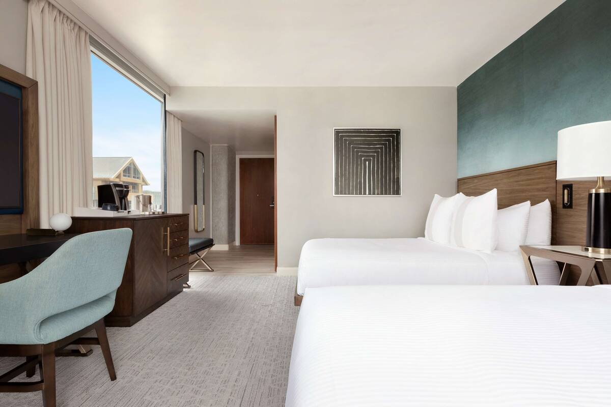 Habitación de hotel con una cama grande, un escritorio con silla, cómoda y vistas a un edificio a través de una ventana.