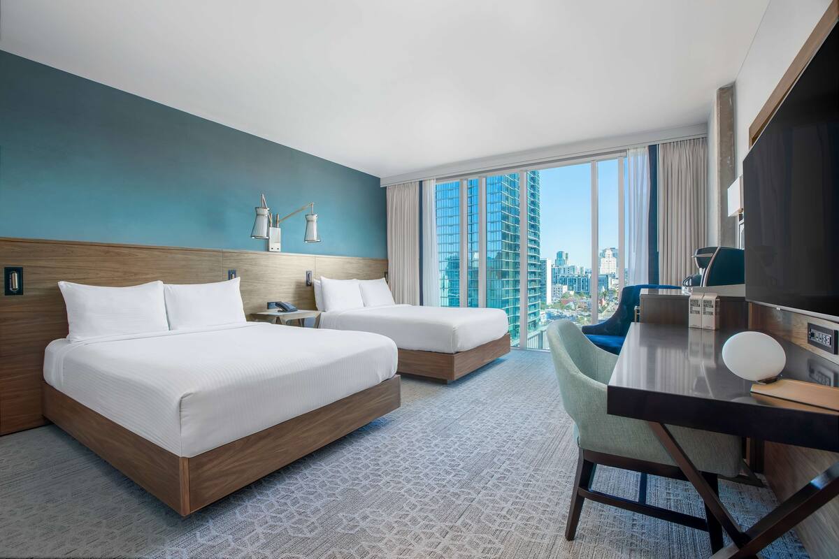 Habitación de hotel con dos camas, un escritorio y vista a la ciudad.