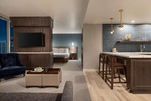 A modern living room with a large TV, dark wood furniture, a blue sofa, and a kitchen area with a bar and stools.