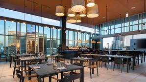 Un restaurante moderno con amplios ventanales, varias mesas para comer y lámparas colgantes.