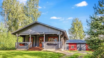 Une cabane en rondins avec un porche, une grange rouge et un ciel dégagé.