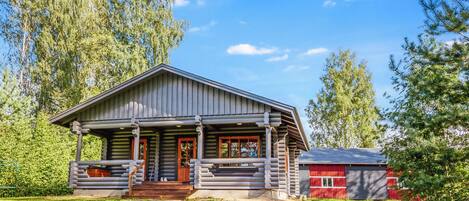 A log cabin with a porch, a red barn, and a clear sky.