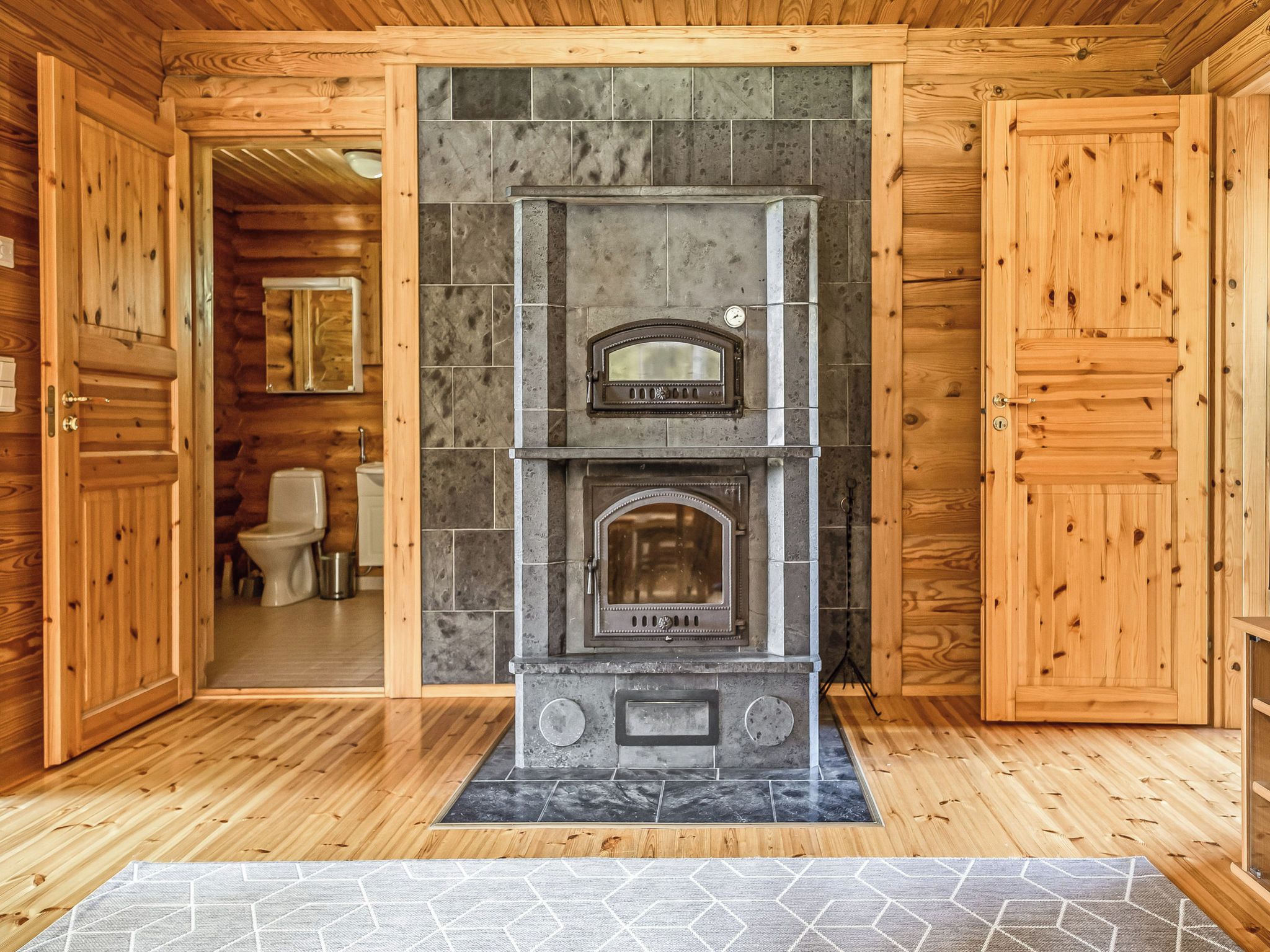 A log cabin interior with a stone fireplace, wooden walls, and a bathroom visible through an open door.