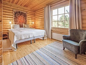 Un dormitorio de cabaña de troncos con cama, dos lámparas de noche, una ventana y una silla.