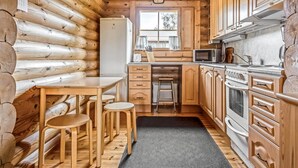 A compact kitchen with wooden cabinetry, a refrigerator, a microwave, and a stove. There is a small dining area with stools and a table. - Marttalanmäki by Interhome (Sysmä)
