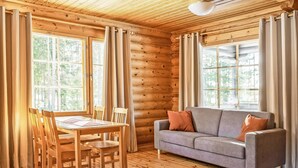 A log cabin interior with a dining table, chairs, a sofa, and large windows. - Marttalanmäki by Interhome (Sysmä)