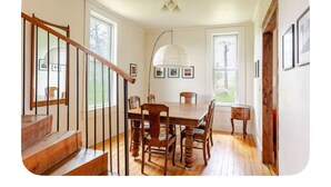 Un espace repas avec une table et des chaises en bois, un escalier avec une rampe en bois et un luminaire suspendu.