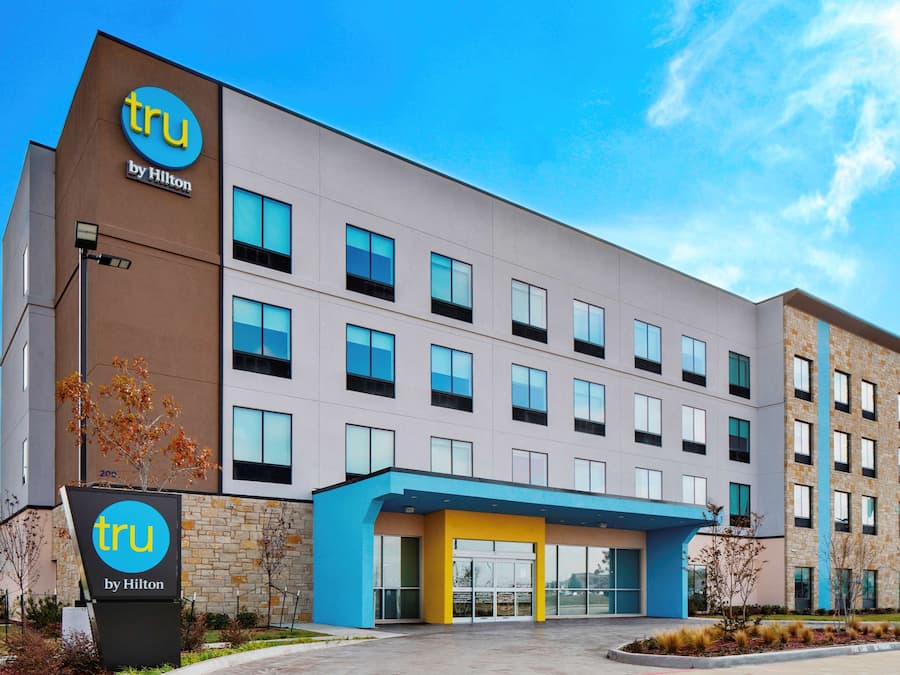 A modern hotel building with a prominent 'tru by Hilton' sign, multiple windows, and a blue entrance area.