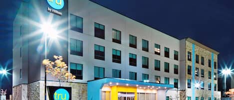 A modern hotel building with a prominent 'tru by Hilton' sign, multiple windows, and a well-lit entrance.