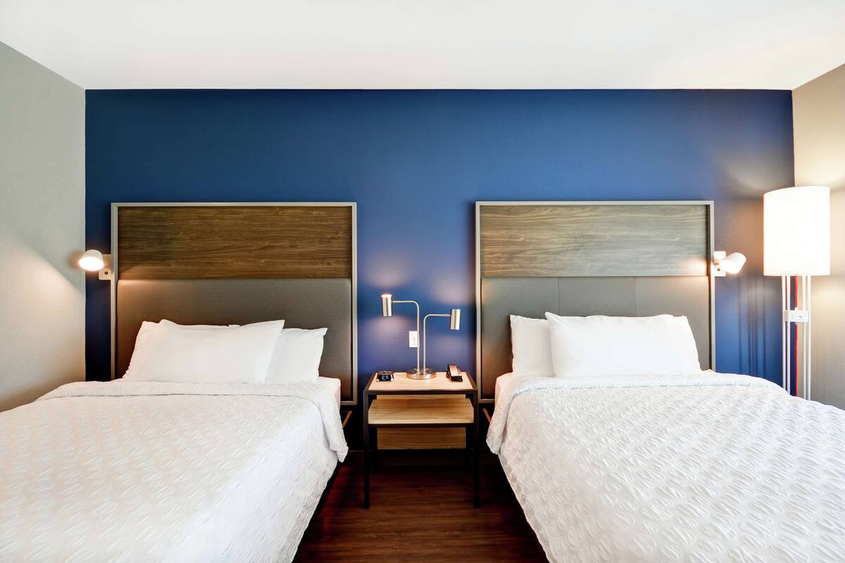A hotel room with two beds, a small table, and bedside lamps.
