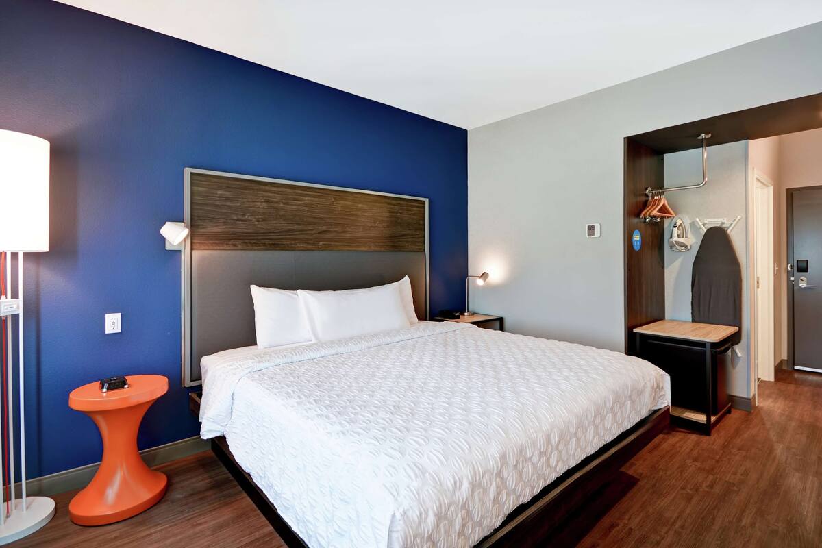 A hotel room with a large bed, a small orange side table, a nightstand, and a mirror.