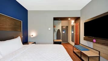 A modern hotel room with a large bed, a bench, a TV, and a walk-in closet.