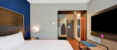 A modern hotel room with a large bed, a bench, a TV, and a walk-in closet.