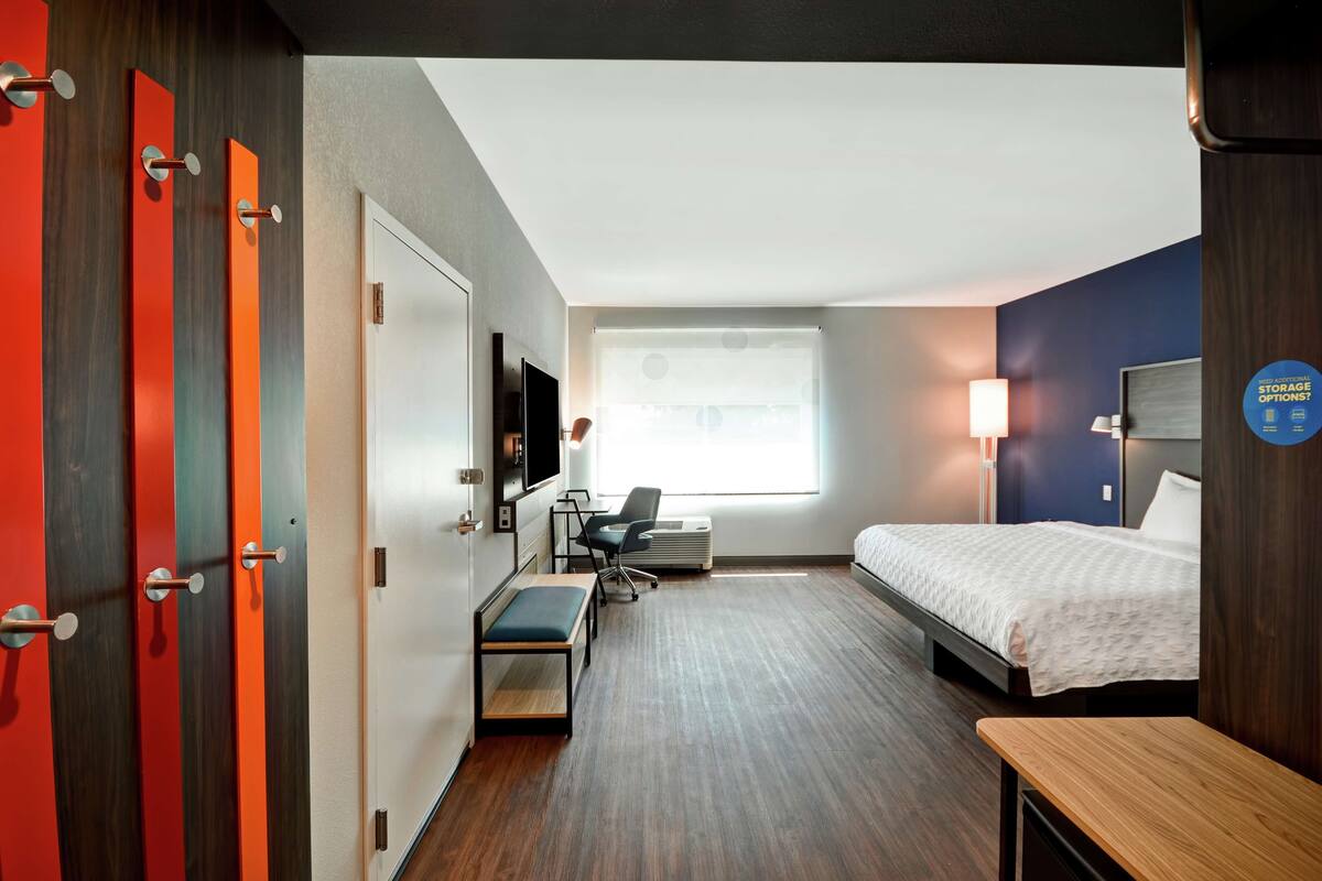 A hotel room with a bed, desk, chair, and a TV.