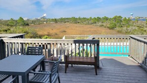 A wooden deck with a pool, outdoor furniture, and a view of a water tower and vegetation. - Perfect Family Vacation Spot in Perdido Key! Private beach access and pool. (Pensacola)