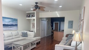 A living room with a sectional sofa, a coffee table, a dining area with a table and chairs, and a ceiling fan. - Perfect Family Vacation Spot in Perdido Key! Private beach access and pool. (Pensacola)