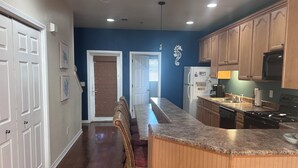 A kitchen with wooden cabinets, a granite countertop, a refrigerator, and a dining area with a chair. - Perfect Family Vacation Spot in Perdido Key! Private beach access and pool. (Pensacola)