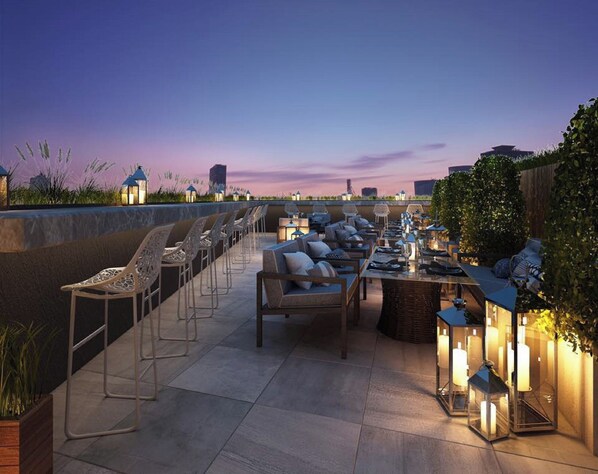 Un espace extérieur aménagé avec des chaises et des tables, entouré de lanternes et de plantes, sous un ciel crépusculaire.