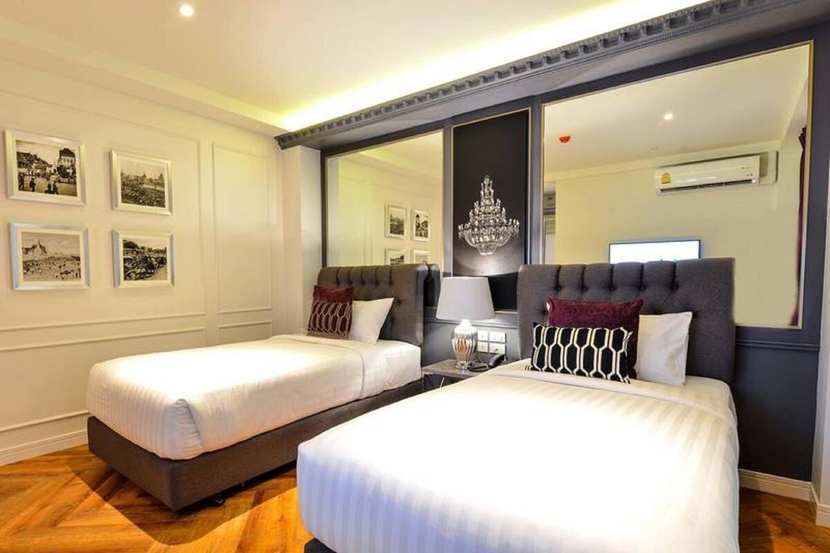 Une chambre d’hôtel avec deux lits, un grand miroir, un lustre et des tableaux encadrés au mur.