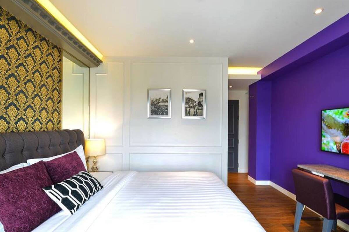Une chambre d’hôtel moderne avec un grand lit, un bureau et un mur d’accent de couleur violette.
