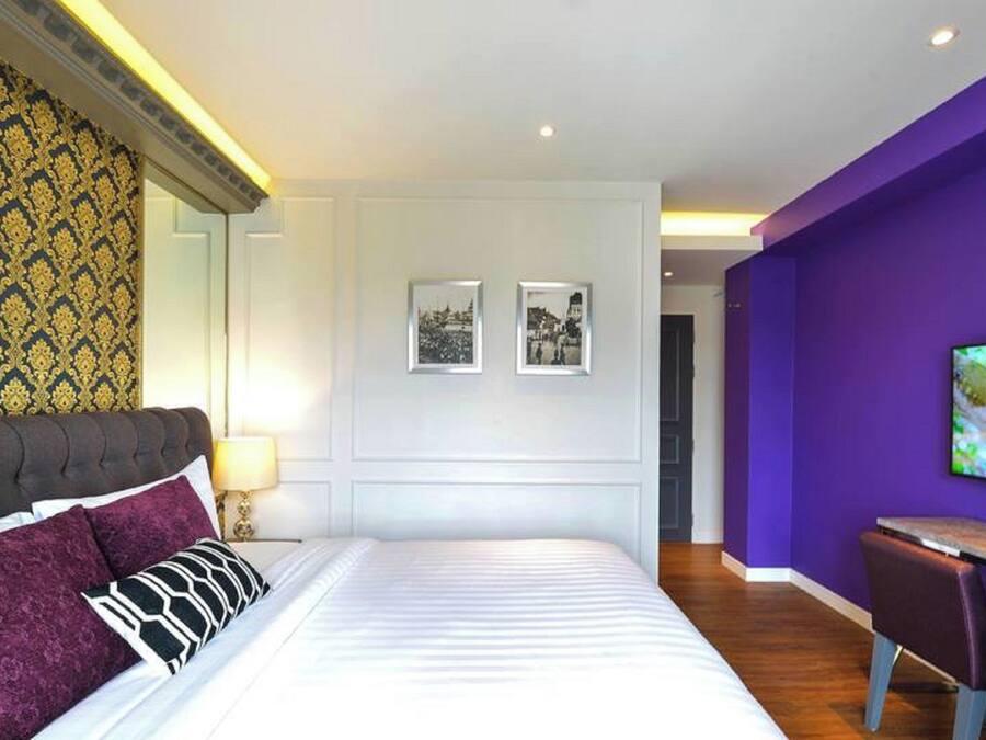 A modern hotel room with a large bed, a desk, and a purple accent wall.