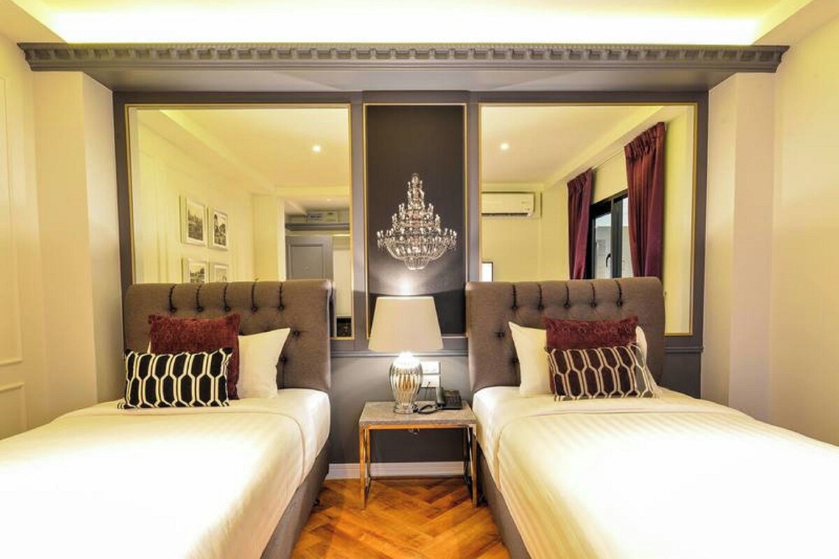 A hotel room with two beds, a chandelier, and a mirror.