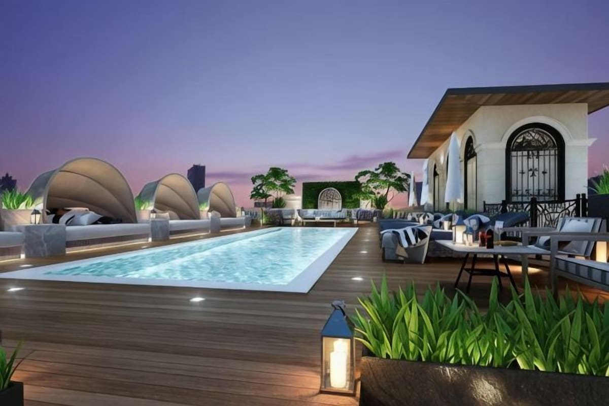 A rooftop pool area with lounge seating and a building with arched windows.