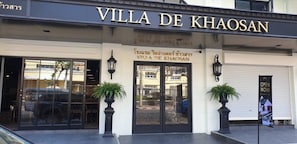 The exterior of Villa De Khaosan with a storefront, entrance doors, and potted plants.