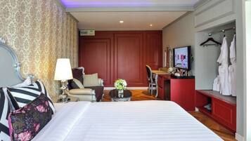 A hotel room with a large bed, a desk, a chair, a TV, and a wardrobe.