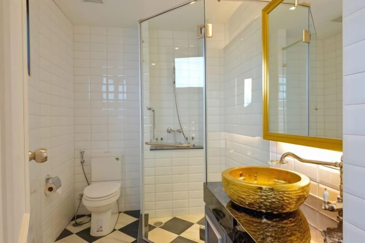 A bathroom with white tiles, a glass shower enclosure, a toilet, and a large, round, textured sink.